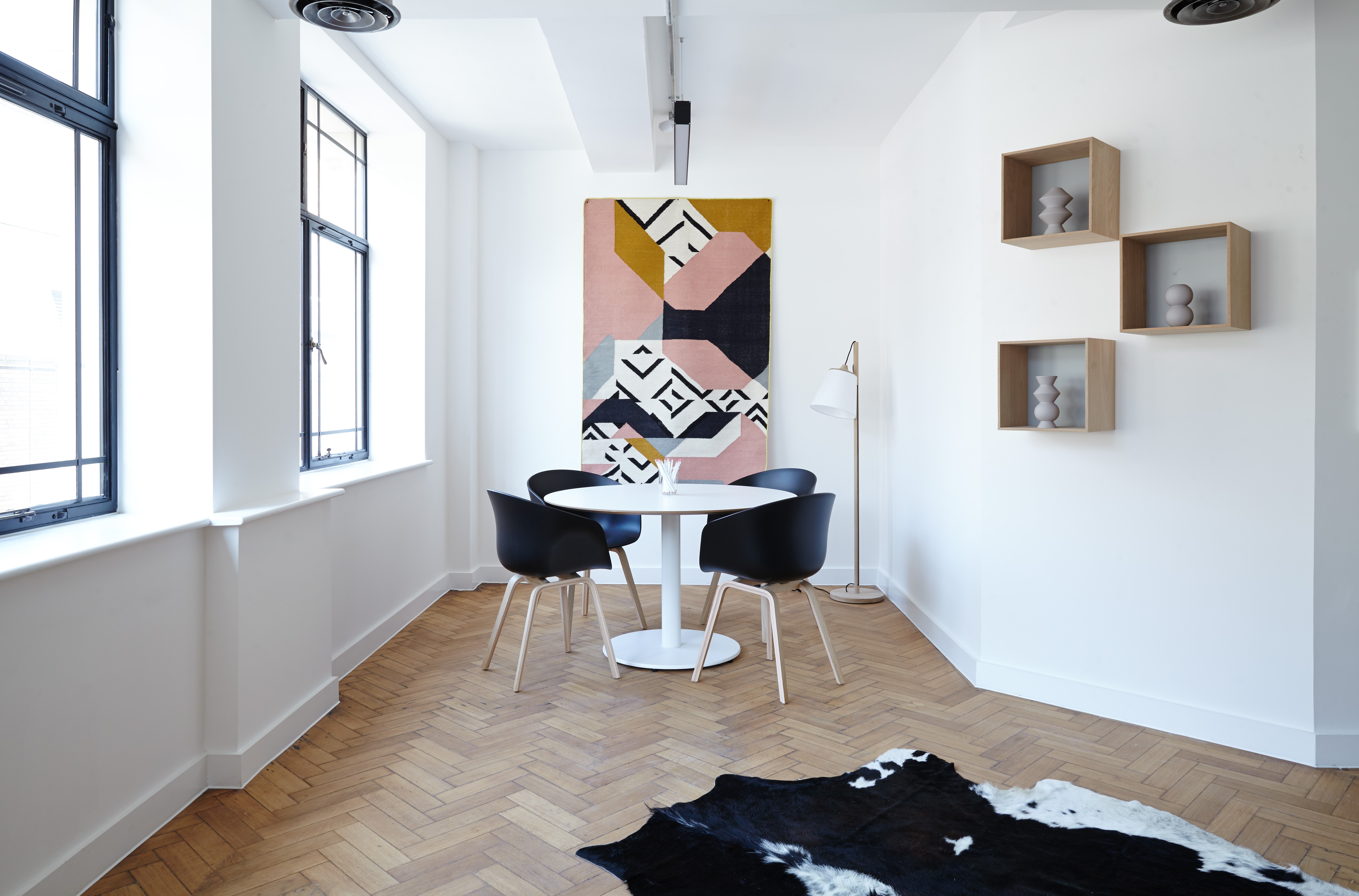 image of an apartment with plenty of natural light, wood flooring, a cowhide rug in the corner, and four black chairs around a circular white table. there are lightboxes and art on the walls.